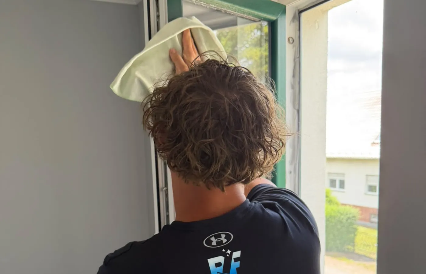 Fensterputzer des Partnerbetriebs wischt den Rahmen eines geöffneten Wohnhausfensters von innen mit dem Tuch nach