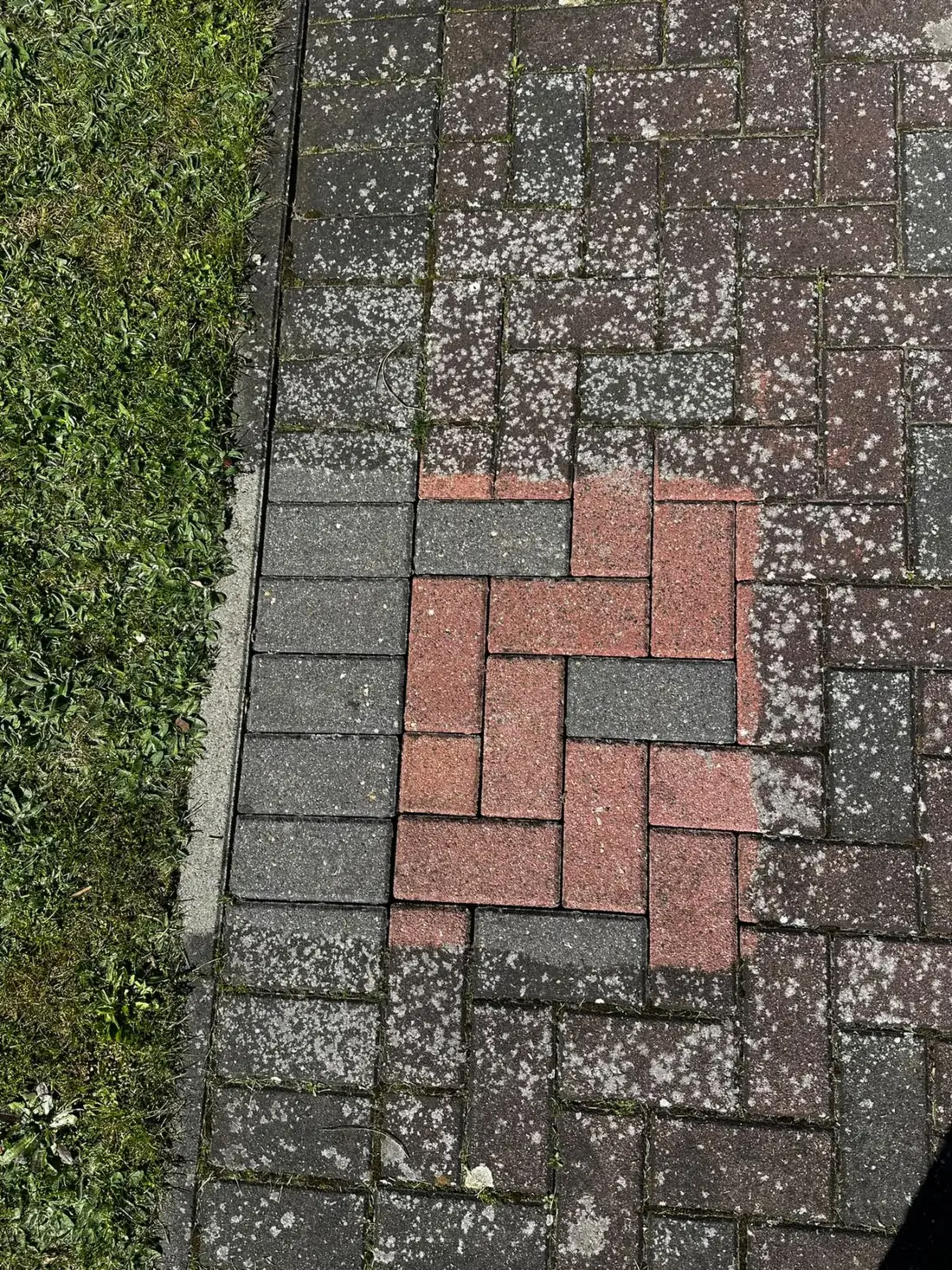 Gepflasterte Fläche mit gereinigtem hellem Quadrat in der Mitte, ringsum grauer Flechtenbewuchs